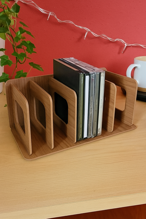 Een lichtbruine houten cd-houder, deels gevuld met cd's, staat op een bureau voor een rode muur met een groene klimop ernaast.