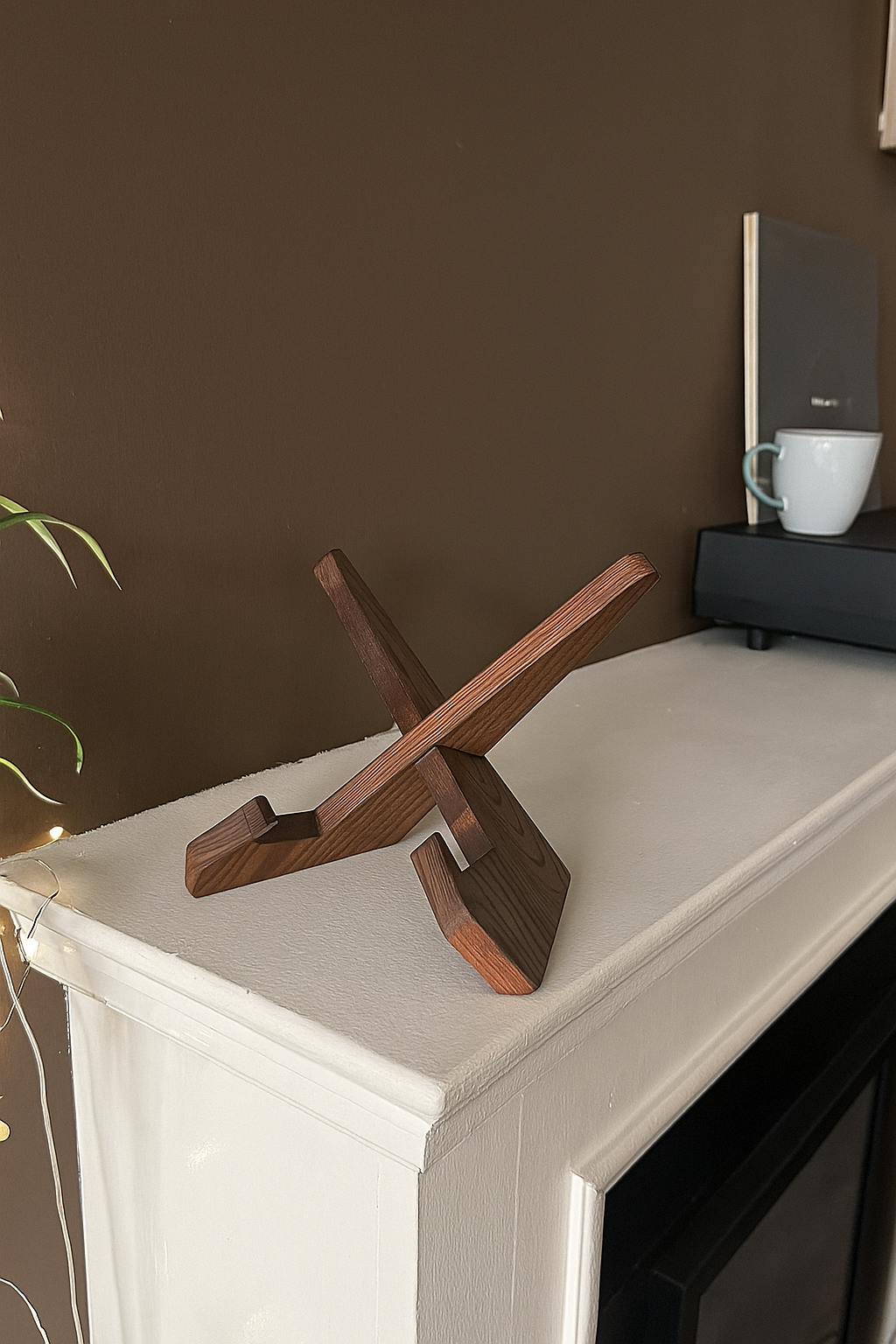 Een donker houten, x-vormige lp-houder staat leeg op een witte schouw in een gezellige woonkamer met een bruine muur.