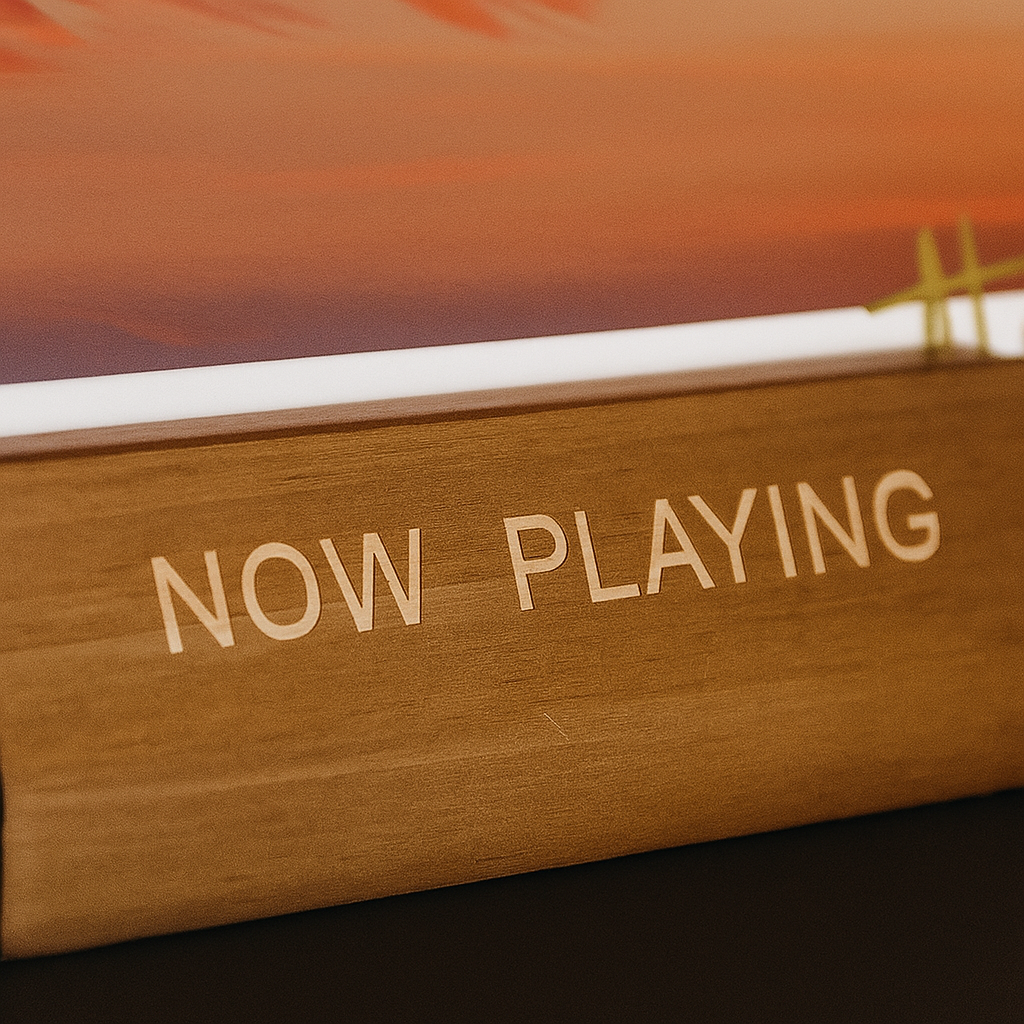 Close-up van de gegraveerde tekst 'NOW PLAYING' op een houten lp-display standaard, waarin een sfeervolle platenhoes zichtbaar is.